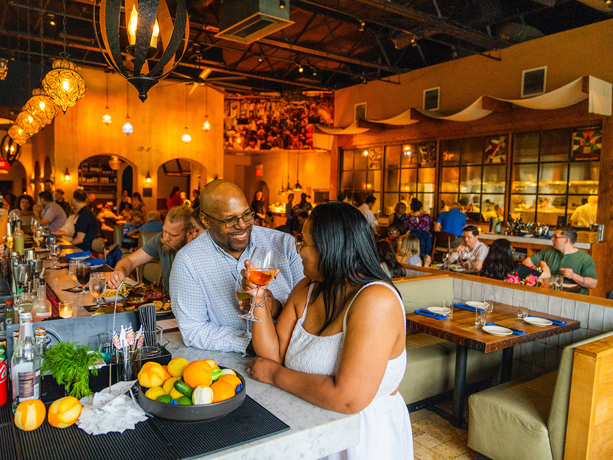 A couple shares a toast at the bar inside Zahav, which features warm lighting, stylish decor and a lively dinner crowd.