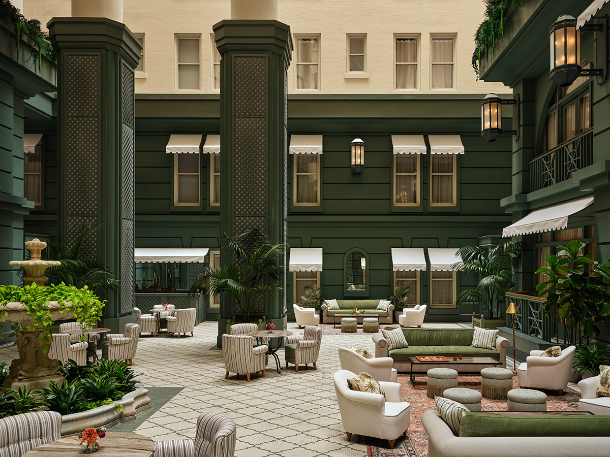A gorgeous interior courtyard space with dark green pillars, white walls, inward looking windows and white furniture at The Bellevue Hotel