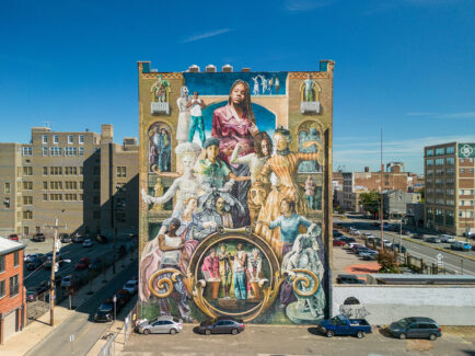 Um grande mural na lateral de um prédio de tijolos retrata pessoas de diferentes épocas e origens conectadas por experiências compartilhadas.