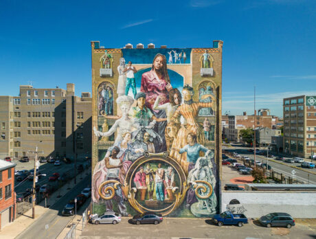 Une grande fresque murale sur le côté d'un bâtiment en briques représente des personnes de différentes époques et origines, liées par des expériences communes.