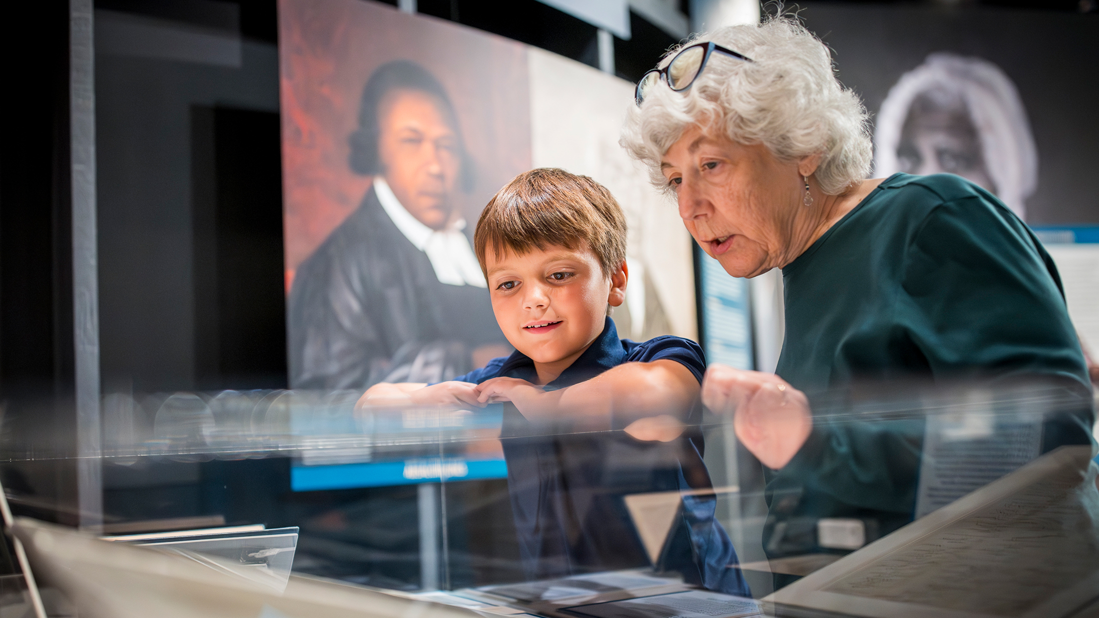 Un niño y una mujer mayor observan de cerca los objetos expuestos en una vitrina de un museo.