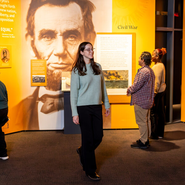 Visitors explore a new exhibit at the Museum of the American Revolution featuring artifacts, text panels and a large image of Abraham Lincoln in the gallery.