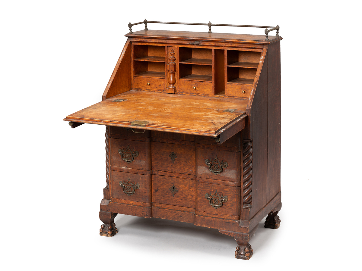 Escritorio de madera del siglo XIX con tiradores de latón y patas de garra sobre fondo blanco.