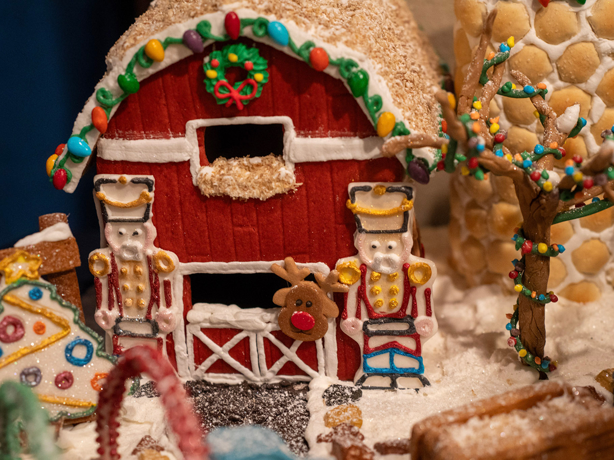 A festive gingerbread barn decorated with candy wreaths, nutcracker figures and a reindeer face surrounded by snow-like icing.