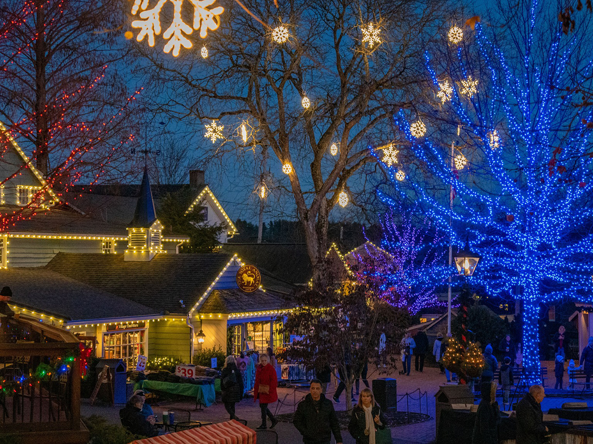 Visitors stroll through Peddler's Village at night, surrounded by glowing holiday lights on the trees and buildings.