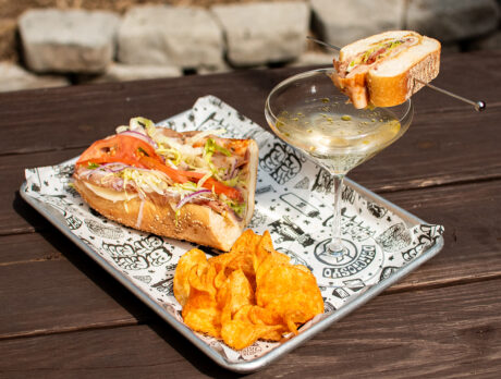 A hoagie sandwich served with chips and a martini garnished with a mini hoagie on a picnic table at Liberty Kitchen.