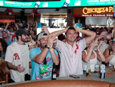 Fans in Phillies jerseys and hats cheer and react with excitement while watching a postseason game on big screens at Stateside Live.