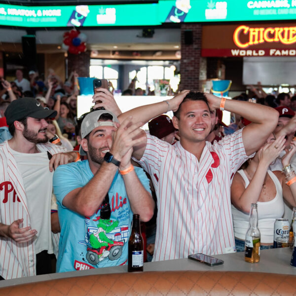 Fans in Phillies jerseys and hats cheer and react with excitement while watching a postseason game on big screens at Stateside Live.