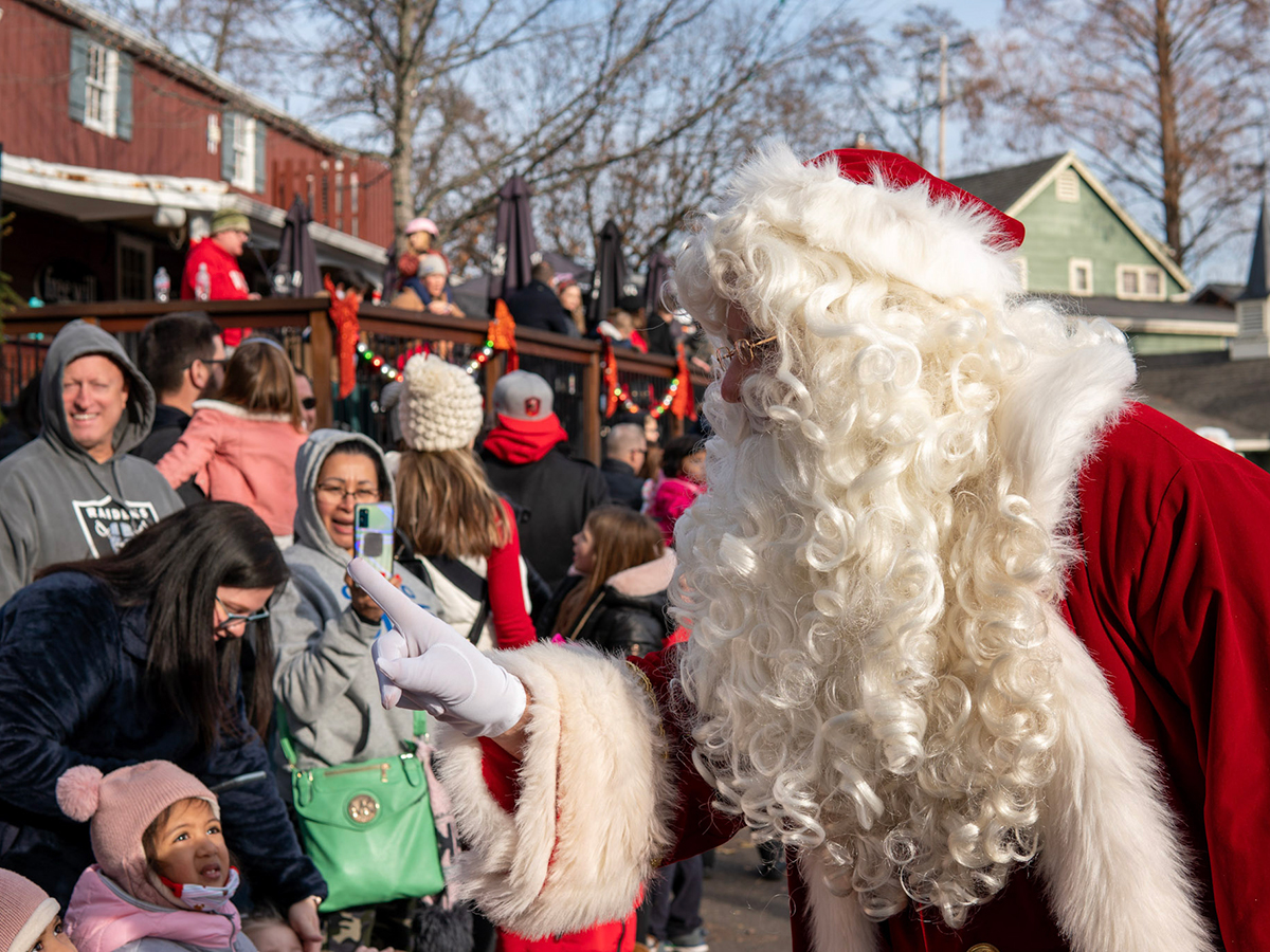 Santa Claus greets a young child and smiles at the crowd during a festive holiday parade at Peddler's Village.