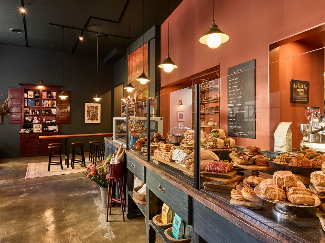 A cozy cafe interior with a pastry-filled counter, warm lighting and seating area for guests.