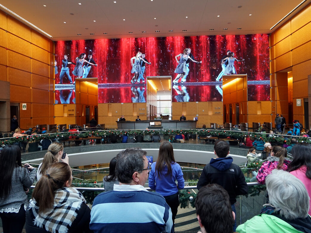 Visitors gather inside the Comcast Center lobby to watch the Comcast Holiday Spectacular, a festive performance displayed on massive LED wall featuring dancers and colorful holiday visuals.