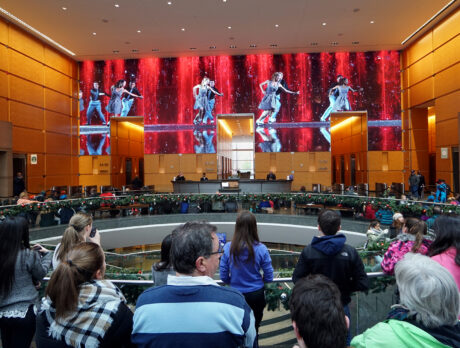 Visitors gather inside the Comcast Center lobby to watch the Comcast Holiday Spectacular, a festive performance displayed on massive LED wall featuring dancers and colorful holiday visuals.