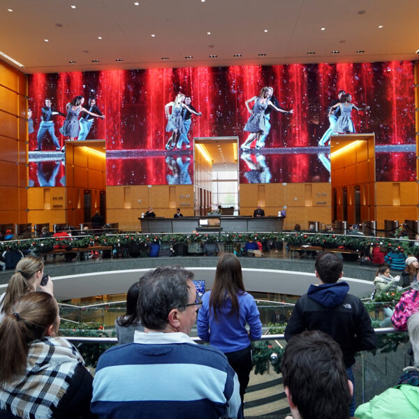 Visitors gather inside the Comcast Center lobby to watch the Comcast Holiday Spectacular, a festive performance displayed on massive LED wall featuring dancers and colorful holiday visuals.