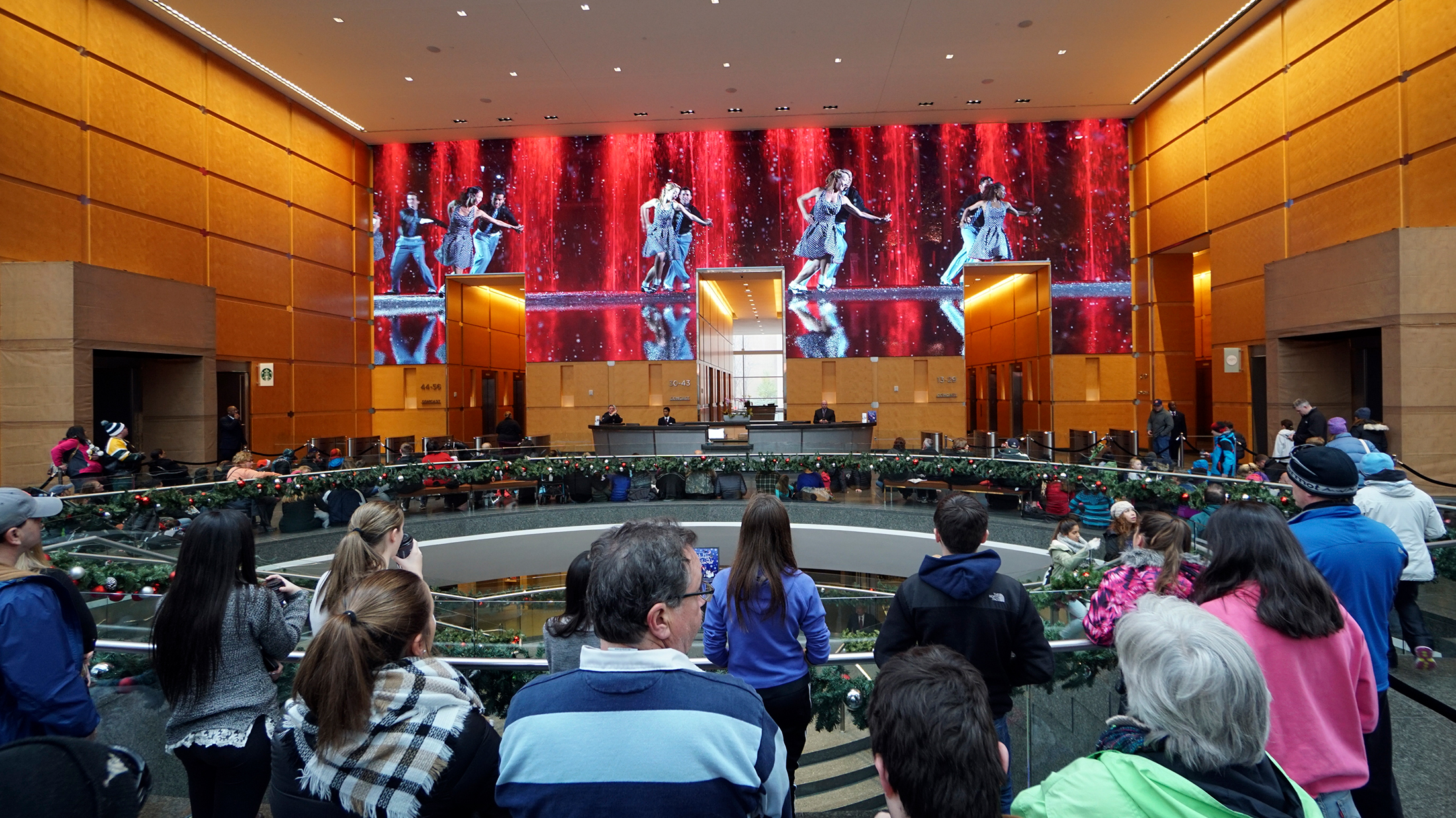 Visitors gather inside the Comcast Center lobby to watch the Comcast Holiday Spectacular, a festive performance displayed on massive LED wall featuring dancers and colorful holiday visuals.