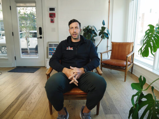Former Eagles player Connor Barwin is seated in a room with plenty of daylight. He is surrounded by several green, leafy plants.