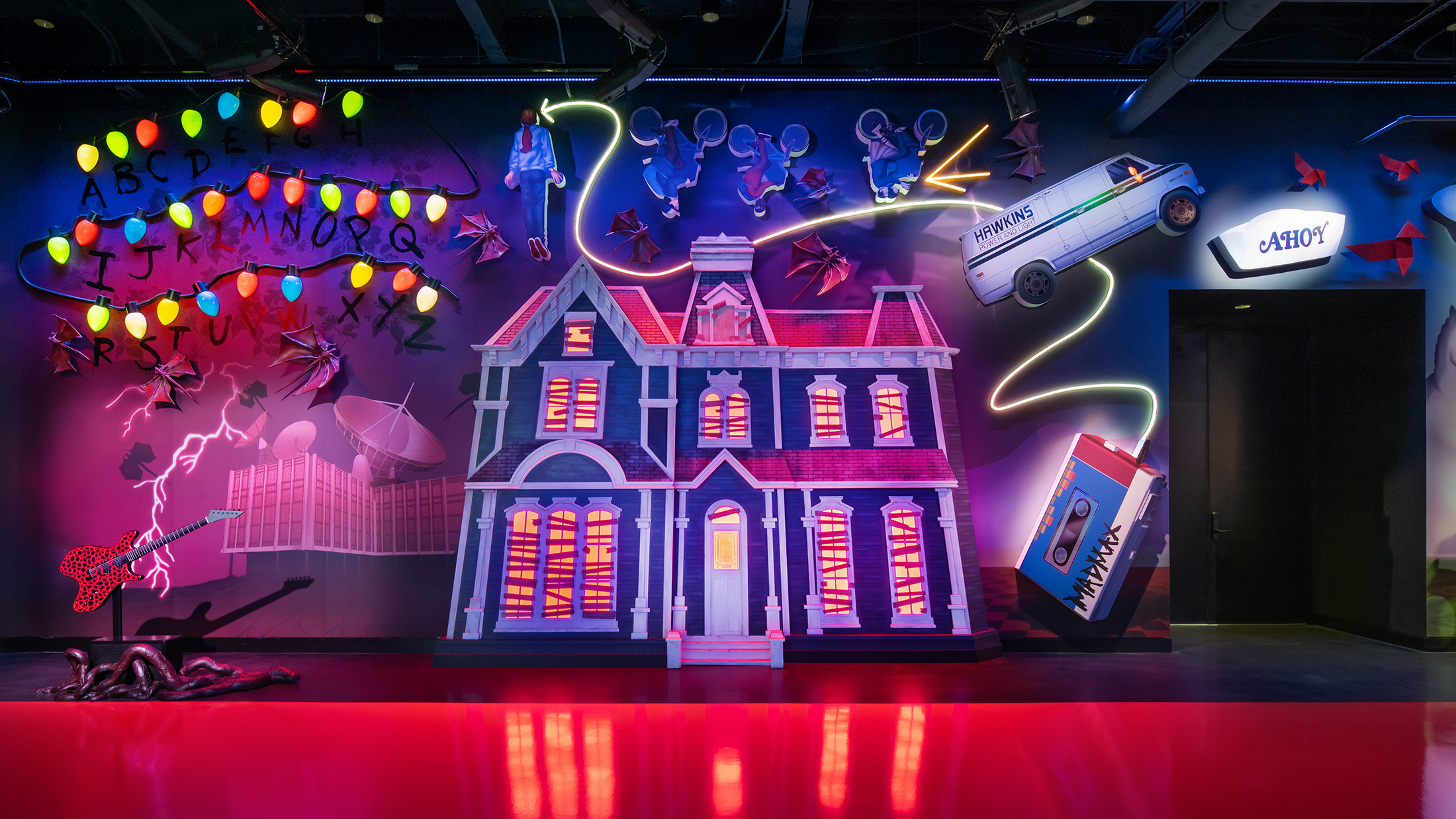 A whimsical, immersive mural featuring Stranger Things inspired lights, flying paper birds, characters on bicycles and a glowing haunted house facade, illuminated with bold neon colors.,