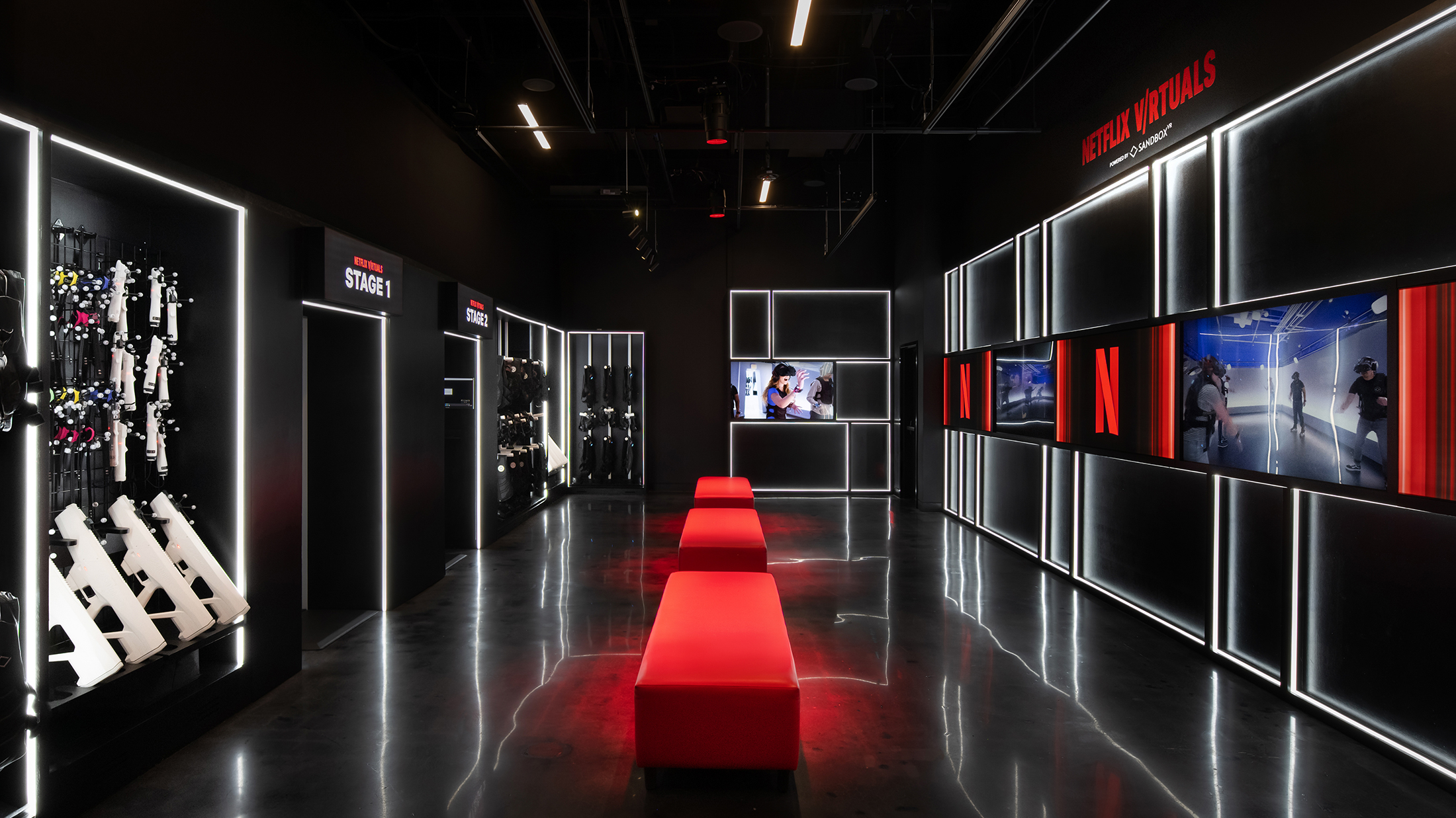 A black neon-lit room with red benches and illuminated walls where guests can engage in immersive VR experiences.