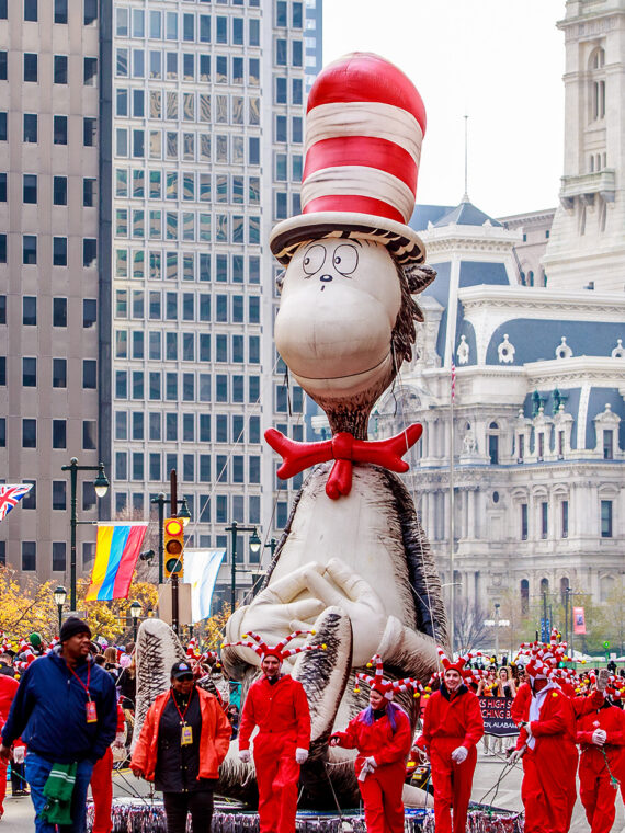 Una gran carroza del Gato en el Sombrero recorre el Benjamin Franklin Parkway durante el Desfile de Acción de Gracias en Filadelfia, con el City Hall al fondo y una multitud de personas observando desde las aceras.