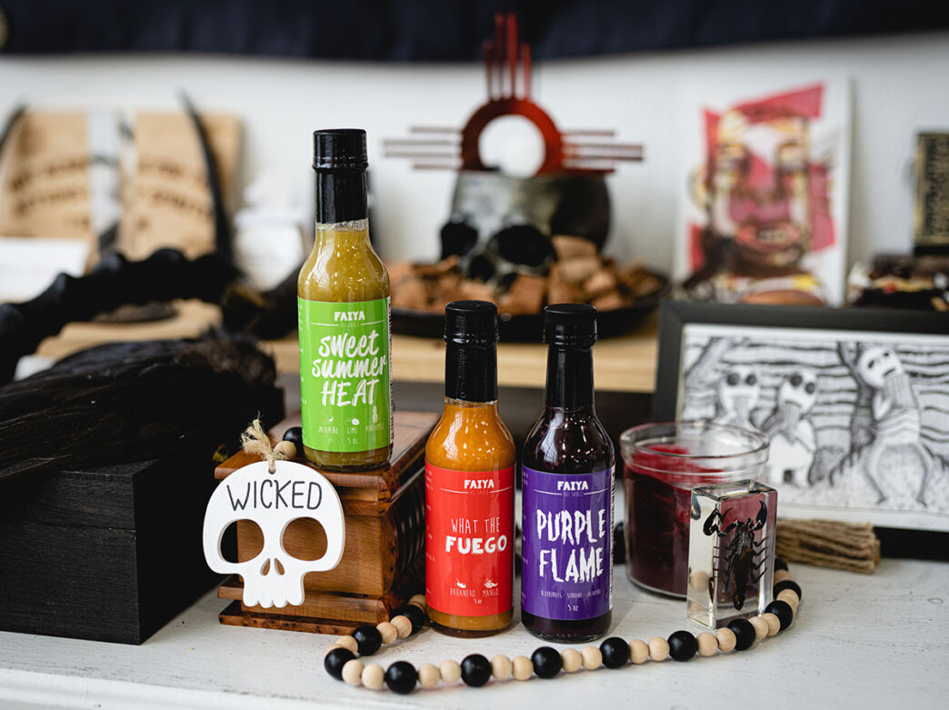 A display of hot sauces with bright labels sit among handmade art pieces, beads and decorative items.