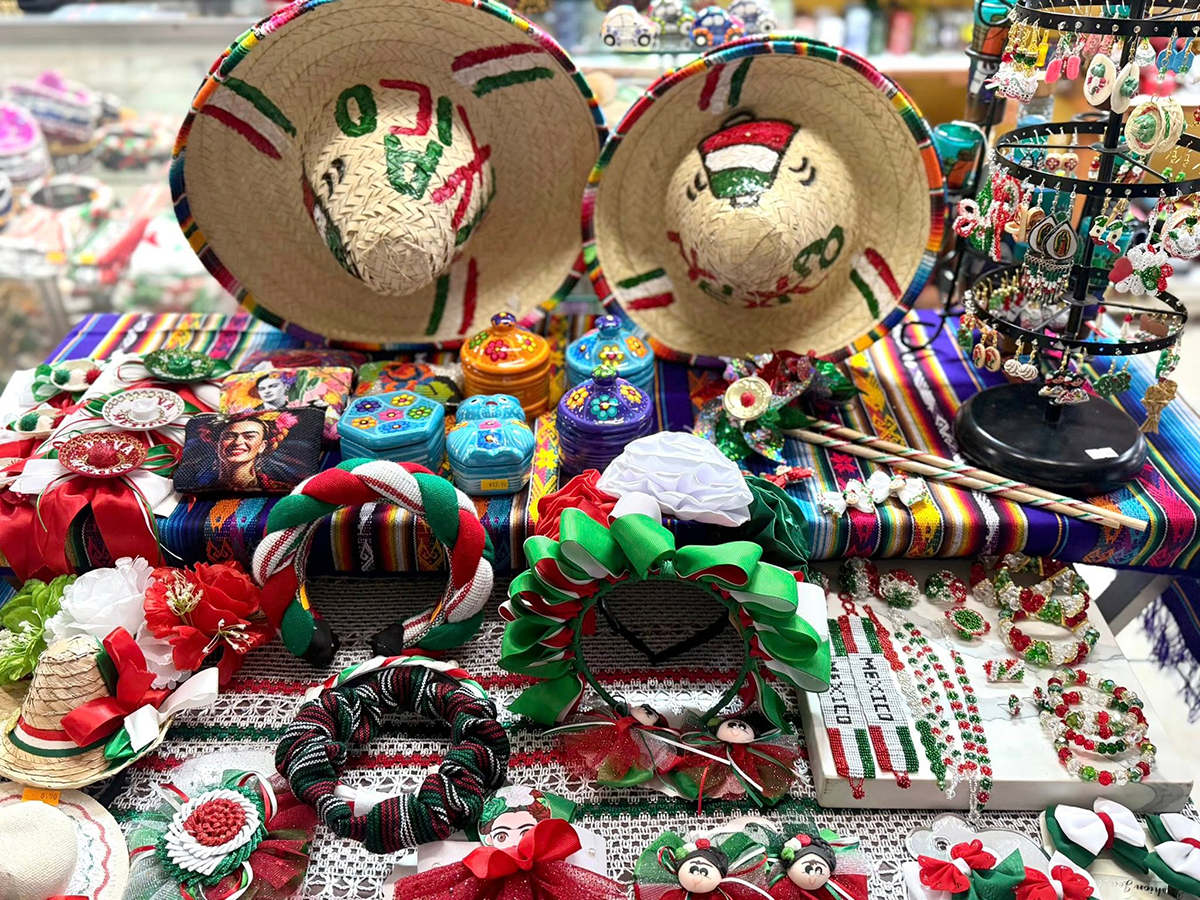 Uma mesa colorida repleta de itens culturais mexicanos, incluindo sombreros bordados, joias, acessórios para o cabelo e artesanato.
