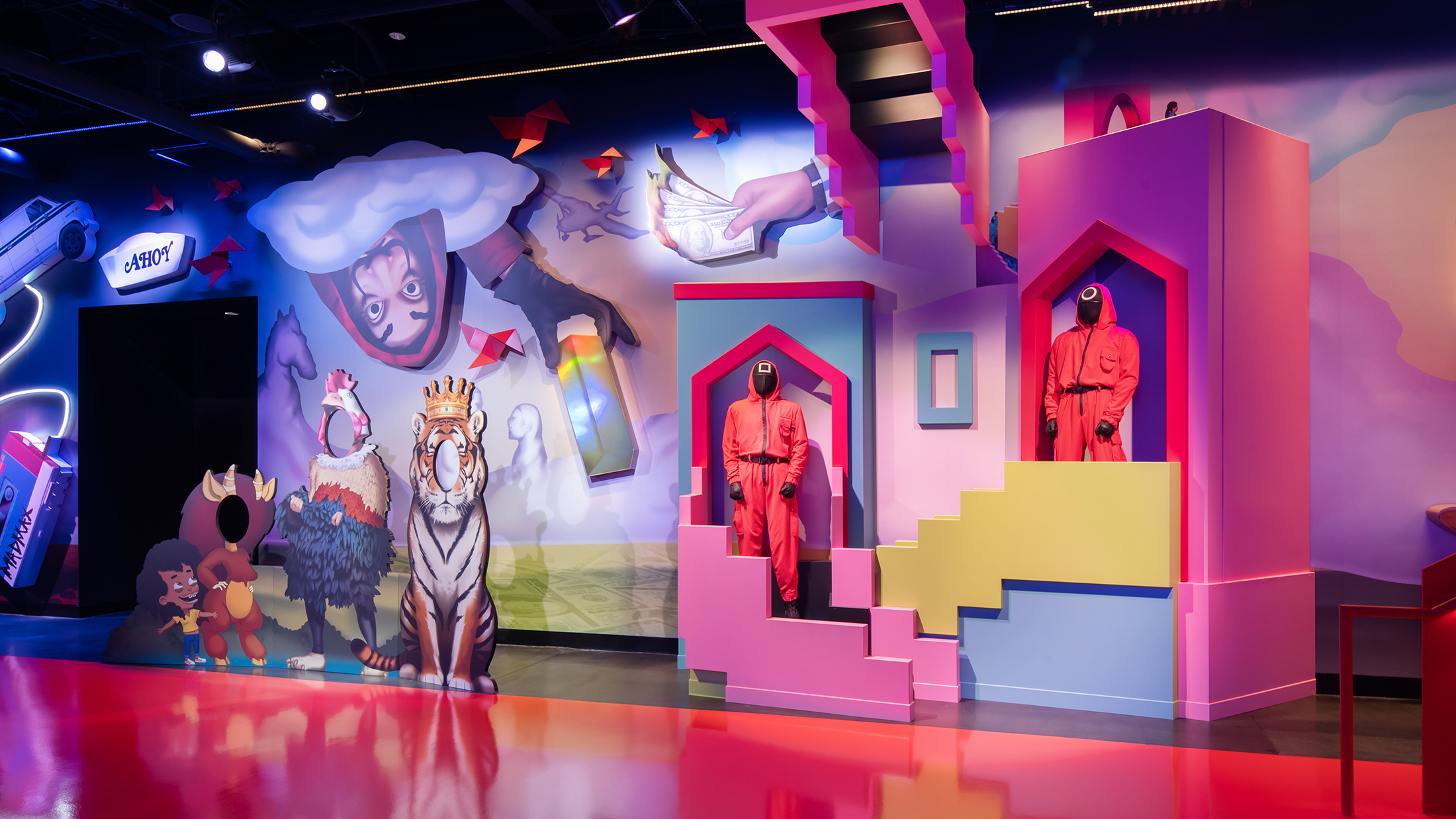 A colorful wall installation with cartoonish cutouts for photo ops and two mannequins dressed in red Squid Game guard uniforms.