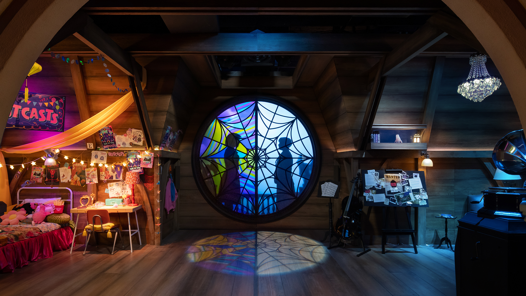 A detailed recreation of a cozy attic dorm room from Wednesday, with one side decorated in warm, colorful teen decor and the other side is decorated with moodier, gothic style.