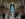 Visitors bundled in winter coats walk through a grand archway of Philadelphia's City Hall toward a massive Christmas tree covered in white lights, framed by tall stone columns.