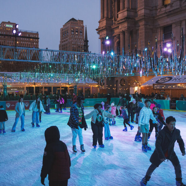Crowds of skaters enjoy an evening on the Rothman Orthopaedics Ice Rink at Dilworth Park, with people gliding across the ice under sparkling silver decorations.