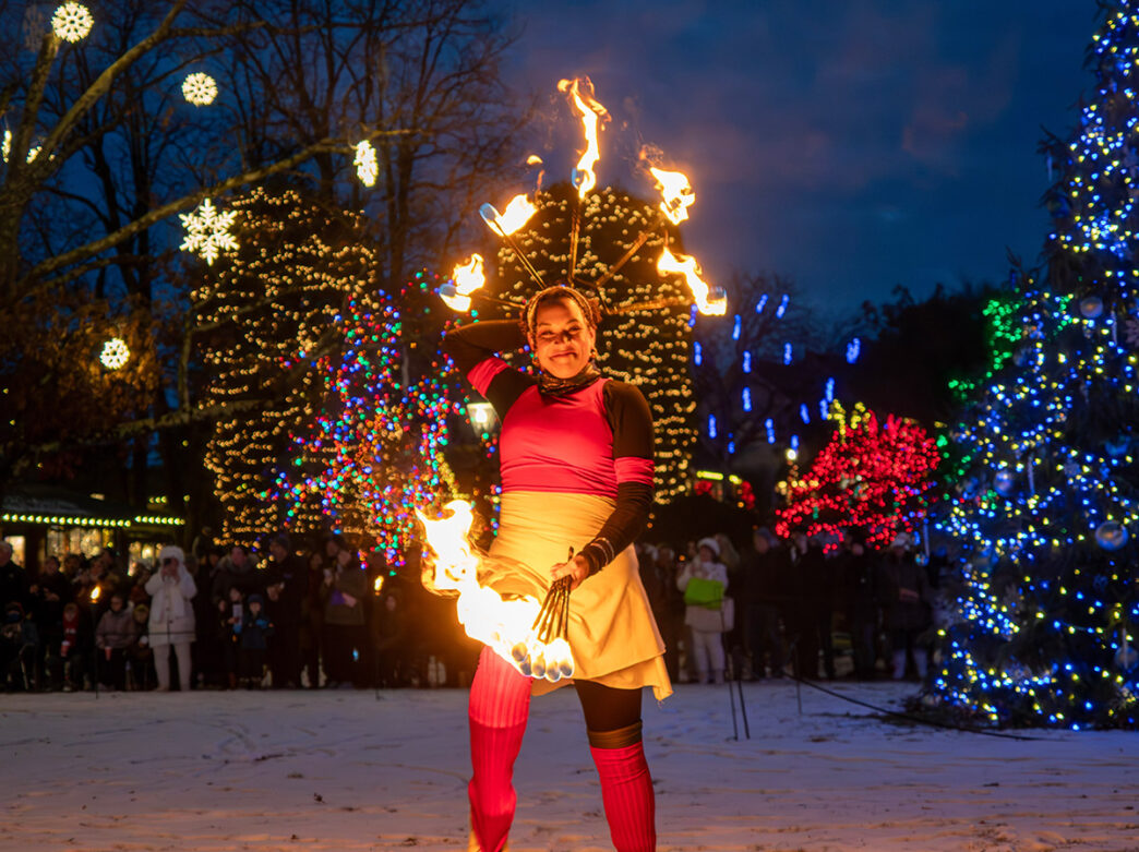 Un artiste brandissant des bâtons enflammés pose pour une photo parmi les arbres illuminés à Peddler's Village.