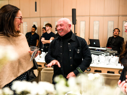 A man in a black coat speaks to a woman during a networking event.