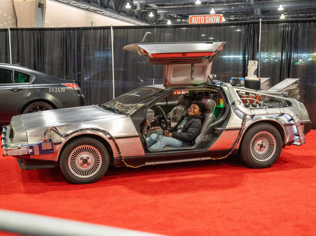 A young boy smiles and sits in the driver’s seat of a DeLorean time machine replica from “Back to the Future."