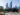 People walk by an outdoor sculpture with the Philadelphia skyline in the background on a sunny day.