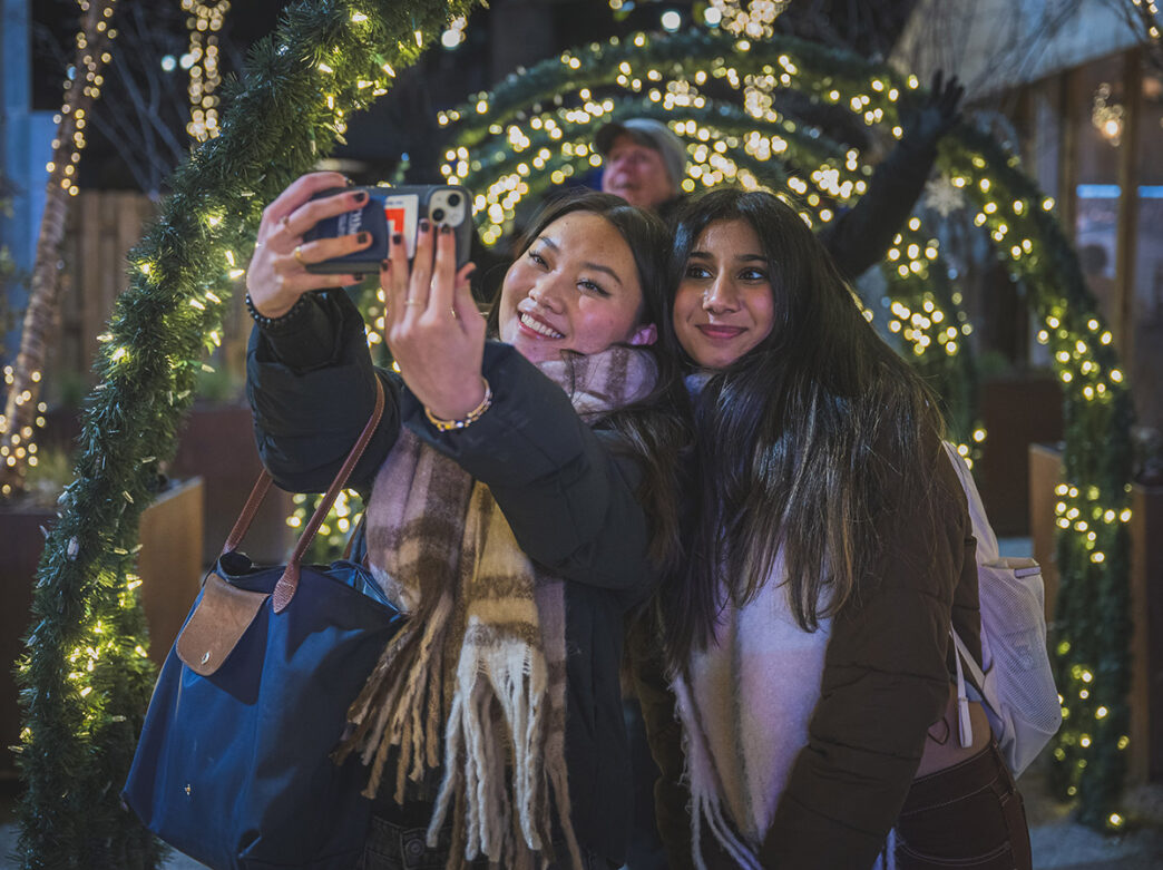 Deux amis chaudement vêtus prennent un selfie devant un tunnel de lumières.