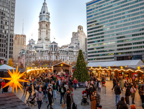 People explore the huts and shops at Christmas Village in Philadelphia, with City Hall in the background
