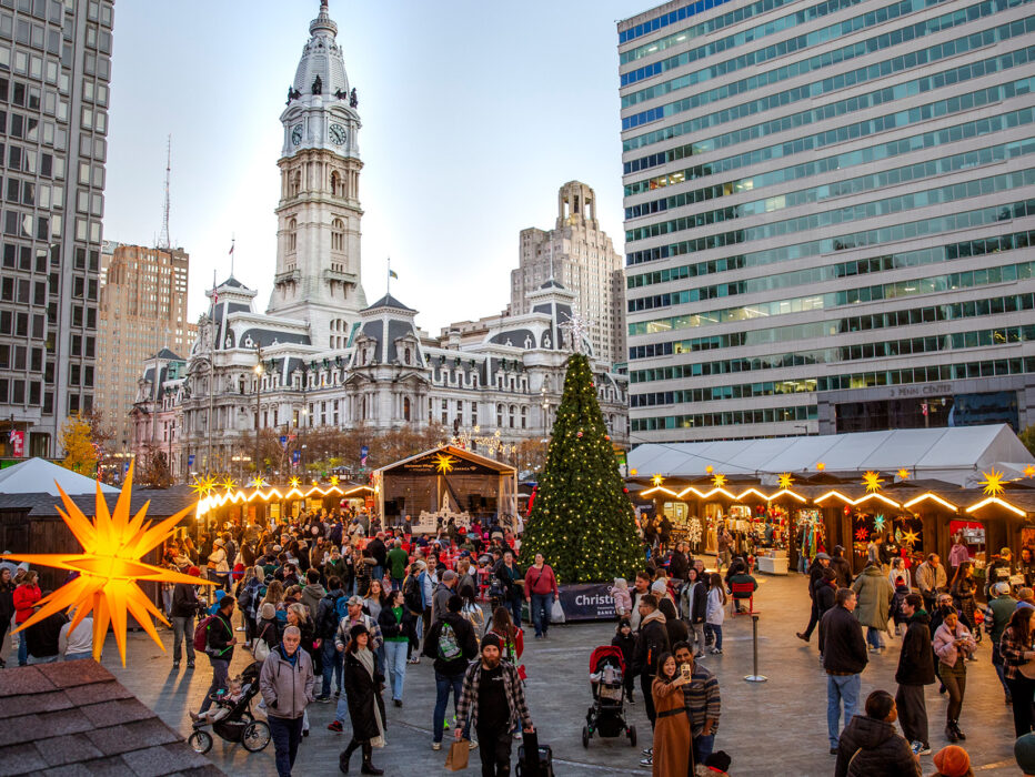People explore the huts and shops at Christmas Village in Philadelphia, with City Hall in the background