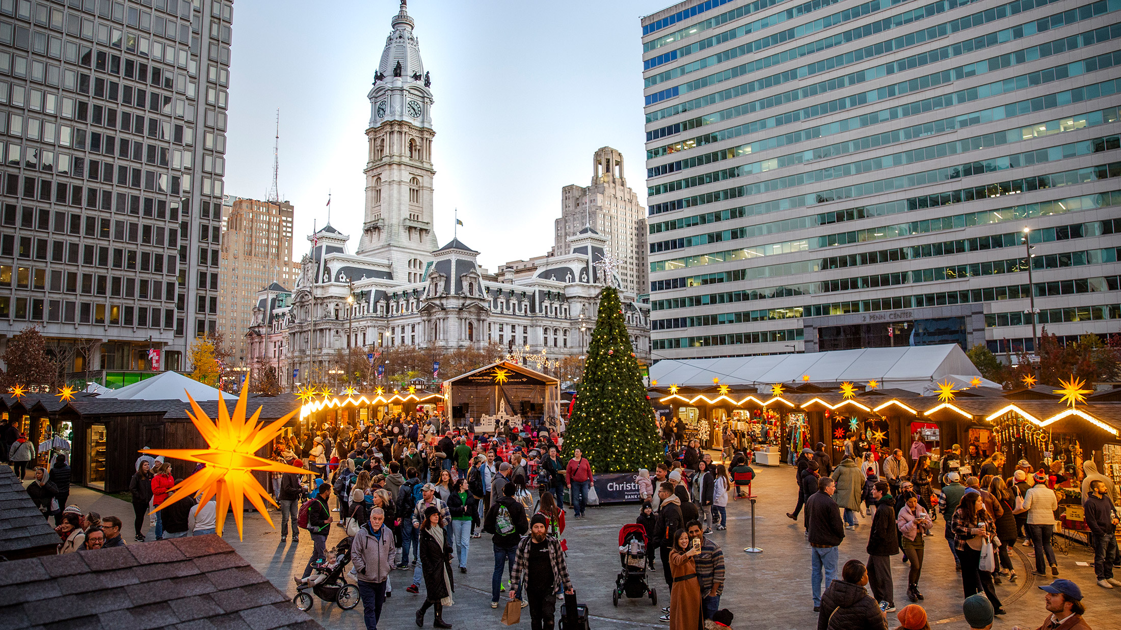 People explore the huts and shops at Christmas Village in Philadelphia, with City Hall in the background