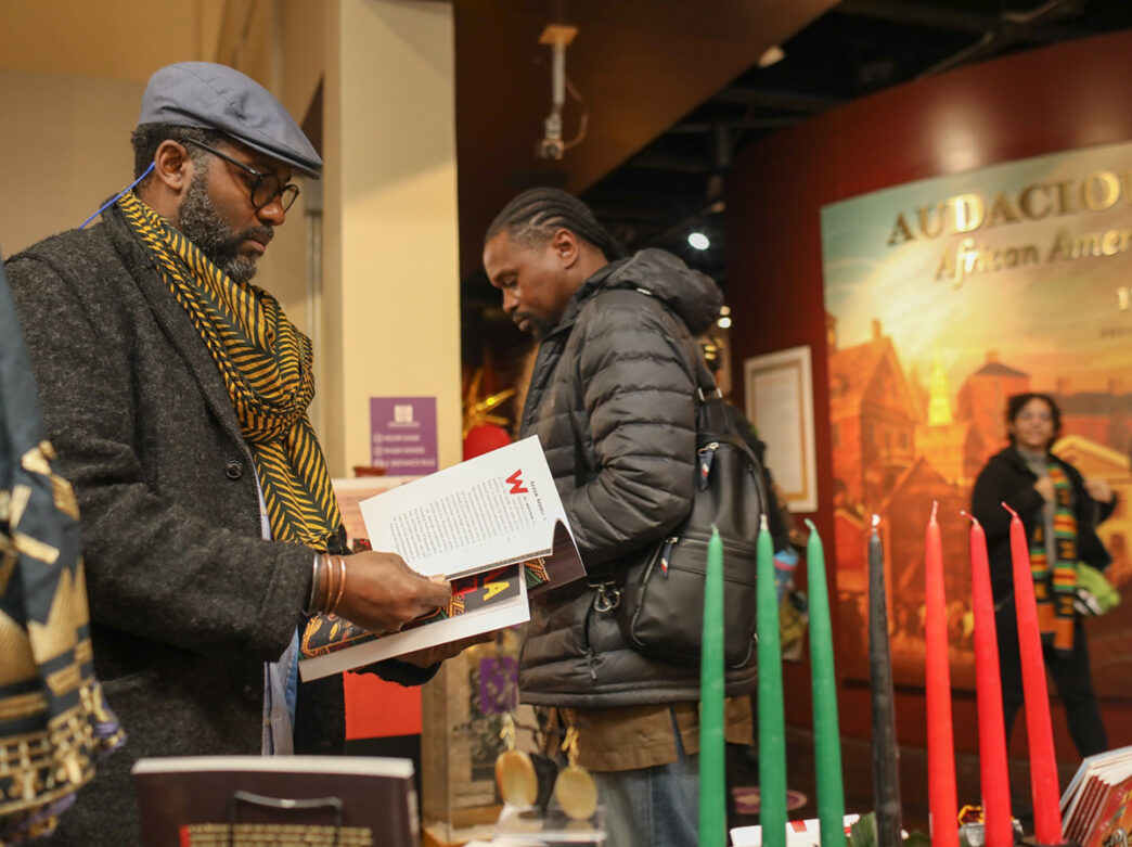 Visitors browse books at a table inside the African American Museum in Philadelphia, with a kinara of red, black and green Kwanzaa candles displayed in the foreground.