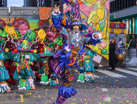 A guy dressed in very colorful attire leaping into the air while confetti falls and a band plays