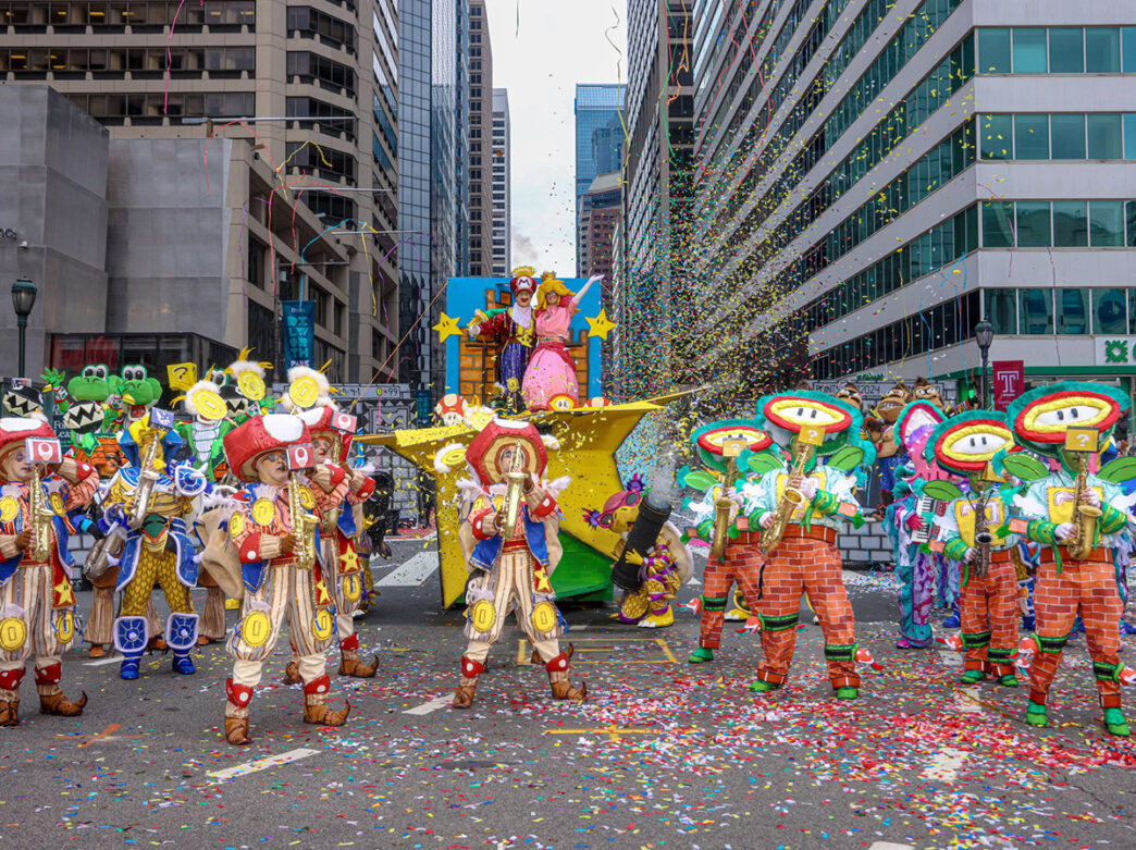 An ensemble dressed as Mario characters (mushroom, flower, princess and more), and playing music while confetti falls