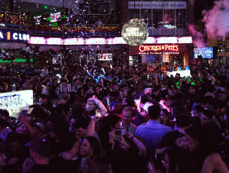 A packed New Year's Eve party with confetti falling, and glowing disco ball overhead and partygoers celebrating under glowing lights.