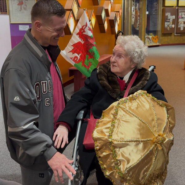 An older woman in a wheelchair speaks with a man kneeling down beside her.