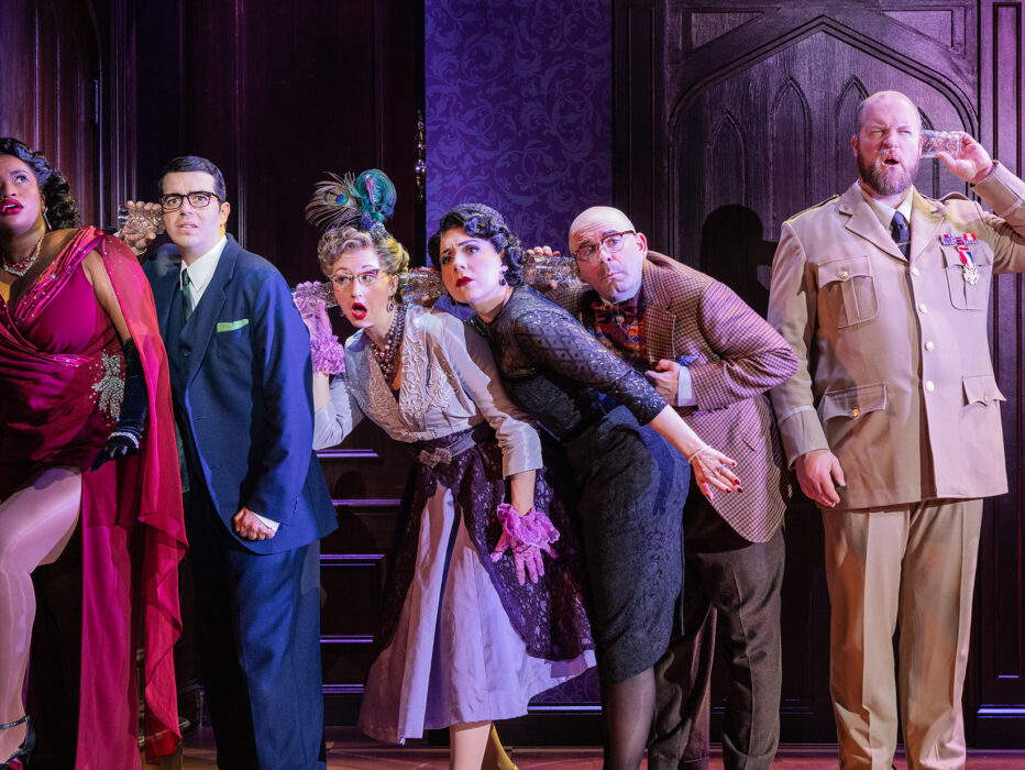 Cast members in period costumes lean in while holding glass cups to their heads to try to listen to the room next door during the production of Clue.