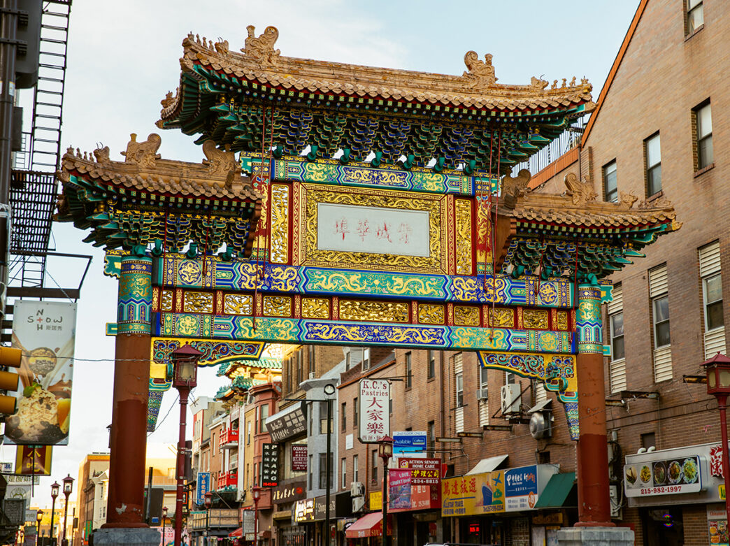 Philadelphia's ornate Chinatown Friendship Gate rises above a busy street lined with shop and restaurants, featuring colorful tiles, carved dragons and traditional Chinese architectural details.