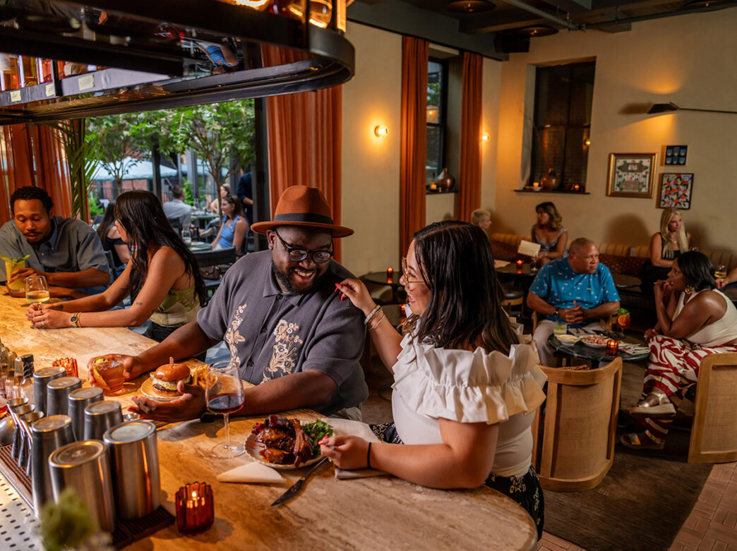Three couples talk and eat in the dining room of the restaurant Bastia, inside of Hotel Anna & Bel.