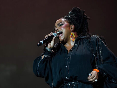 Jill Scott canta em um microfone enquanto se apresenta no palco. Seus olhos estão fechados.