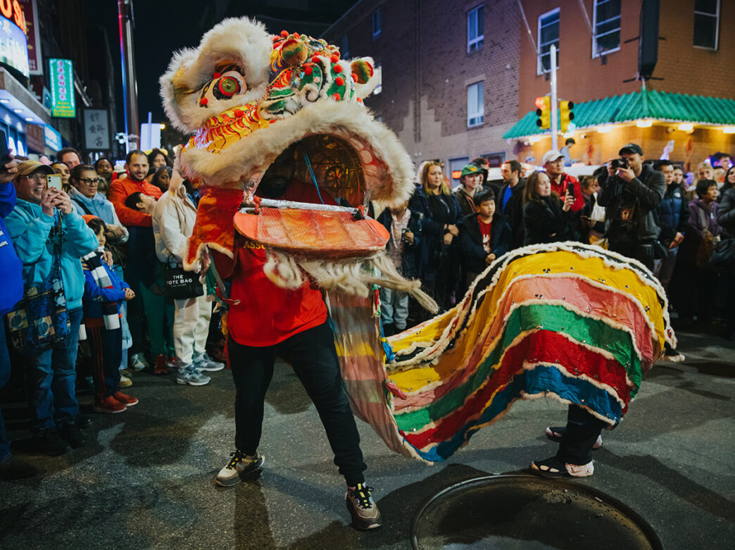 A colorful lion dancer weaves through a crowded city street at night during a Lunar New Year parade in Philadelphia's Chinatown.