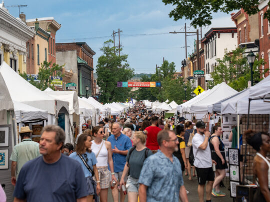 A large crowd shops at white vendor tents lining Main Street at the Manayunk Arts Festival.