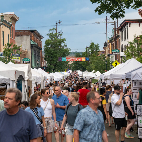A large crowd shops at white vendor tents lining Main Street at the Manayunk Arts Festival.