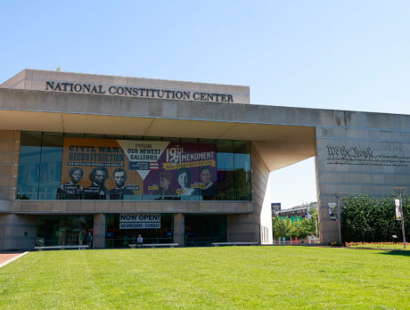 Exterior of National Constitution Center with banner about newest galleries and green grass lawn.