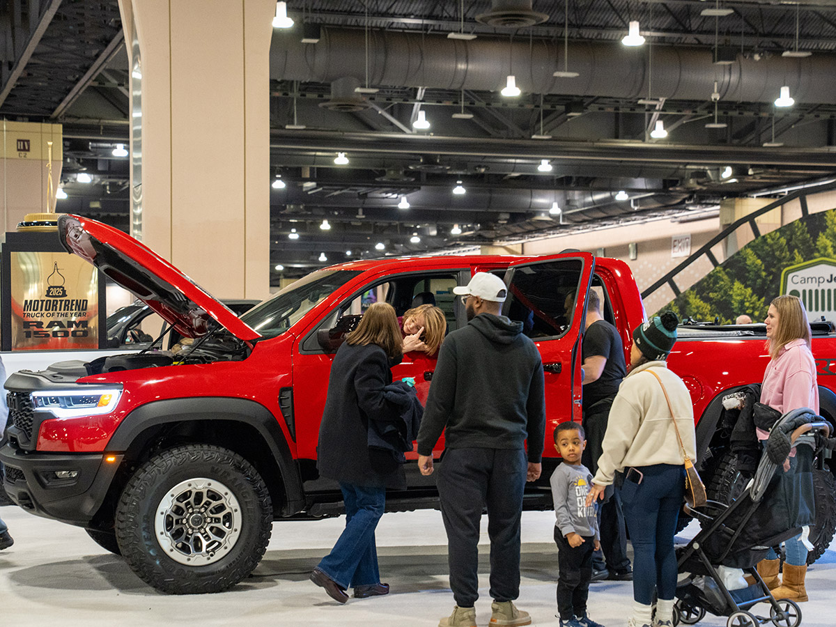 A family of adults and children admires a bright red pickup truck at the Philadelphia Auto Show.